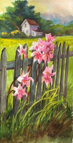 Naked ladies pink flowers in front of a rustic fence with a farmhouse backed by trees in the background