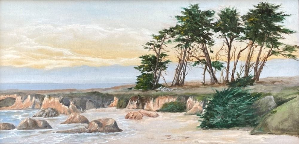 An old grove of cypress trees sit atop the green gray grass of the Pudding Creek headlands overlooking the beach. Yellow late afternoon clouds hang over the sea.
