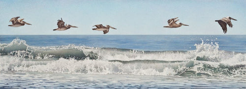 Five brown pelicans flying in formation above the breaking waves, pale blue sky and deeper blue ocean with white and gray toned waves
