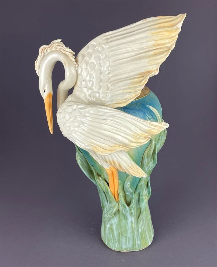 Glorious heron with wings ready to fly on a tall vase adorned with reeds