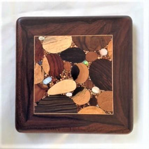 Various woods and shell inlaid into a small square, framed with deep dark wood and a thin pale inlaid line surrounding. 