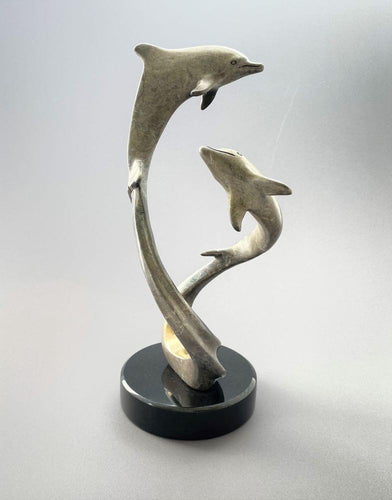 A pair of dolphins swim together, swirling around each other, bronze with grey patina and gold wave. 