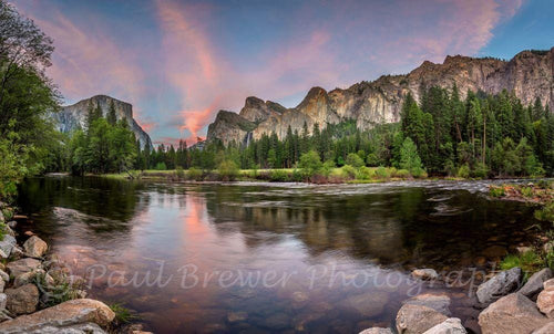 Iconic Yosemite Valley with the Merced River in the foreground and salmon pink clouds at sunset.