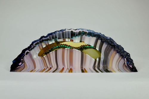 Kiln formed glass sculpture in soft pink, lavender, purple, emerald and gold ribbons of color in an arched shaped piece. The top arched edge is textured with smooth, flat sides and bottom.