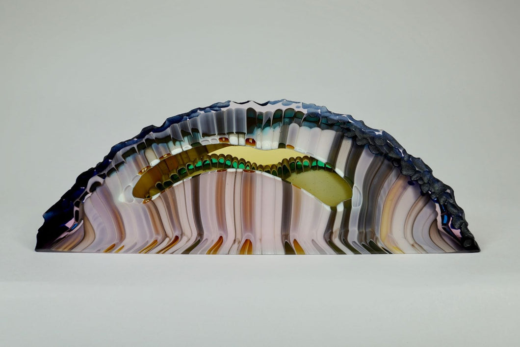 Kiln formed glass sculpture in soft pink, lavender, purple, emerald and gold ribbons of color in an arched shaped piece. The top arched edge is textured with smooth, flat sides and bottom.